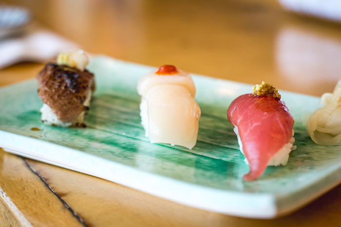 three pieces of sushi with fish on a green plate and a wooden table 