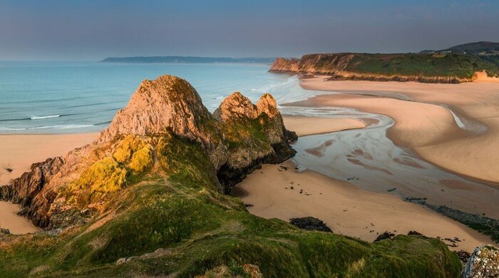 Three cliffs bay in the UK gloomy day beach and river rocks covered with grass and moss