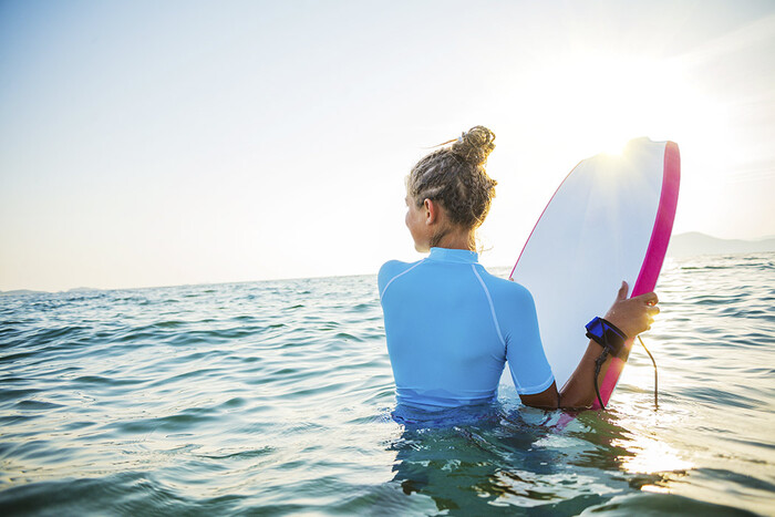 travel and summer sports woman in a white suit with her hair up holding her surf board at sunset in the water