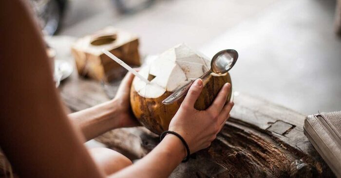 woman and coconut woman holding a spoon with a coconut with a straw in her hands on a wooden table