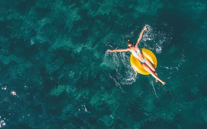 Summertime relaxation woman in the sea floating on a yellow inflatable ring with her hands spread