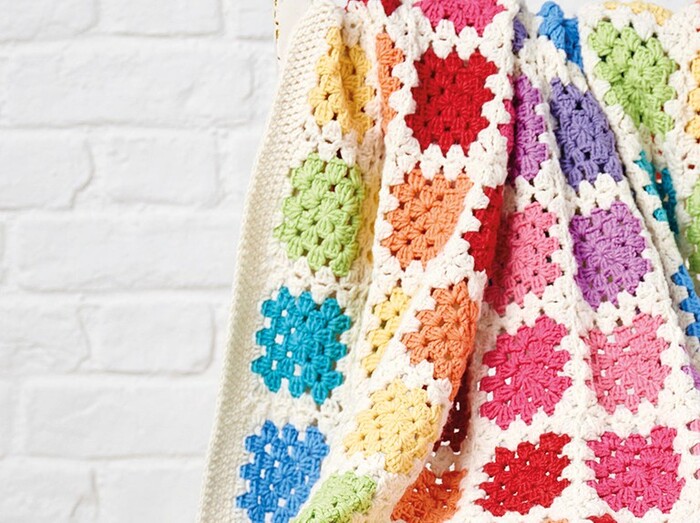 crochet blanket colorful square patterns throw on a white brock wall background