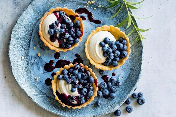 delicious blueberry desserts three baked baskets in a light blue plate with white cream and jam topping