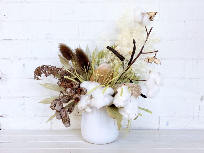 dried flowers in a white vase on a white surface with a white wall in the background 