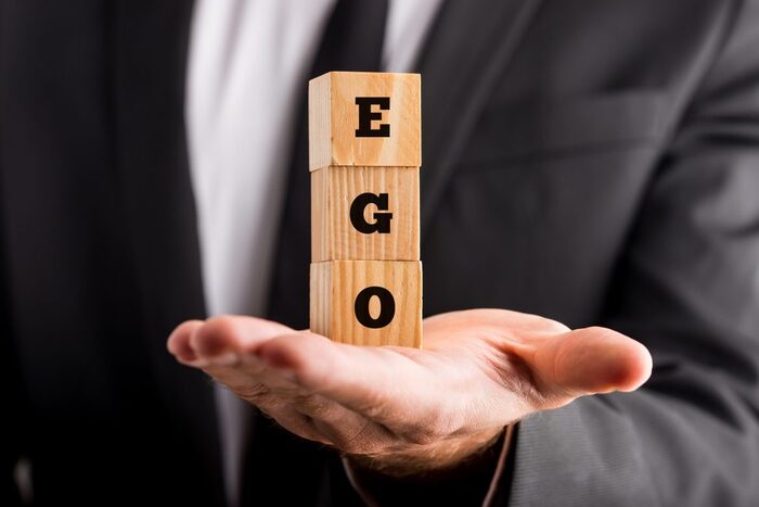 man in a suit holding three wooden cubes with the word ego written on them in black letters