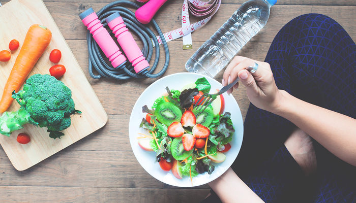 food and workout woman eating from a bowl with veggies and fitness gear around