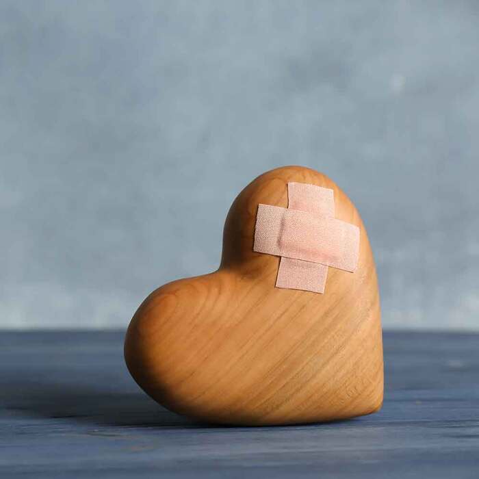 wooden heart lying on a grey surface on a blue wall background with a band aid on