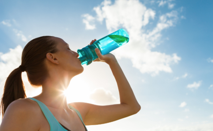 hydration woman in a sports wear with her hair in a pony tail drinking from a large water bottle 