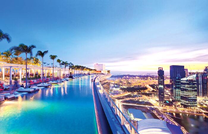 infinity pool singapore Marina bay hotel pool with palm trees and lounge chairs overlooking the city in the evening