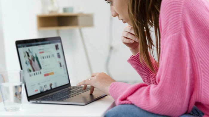 woman in a pink sweater looking online on a computer and shopping 