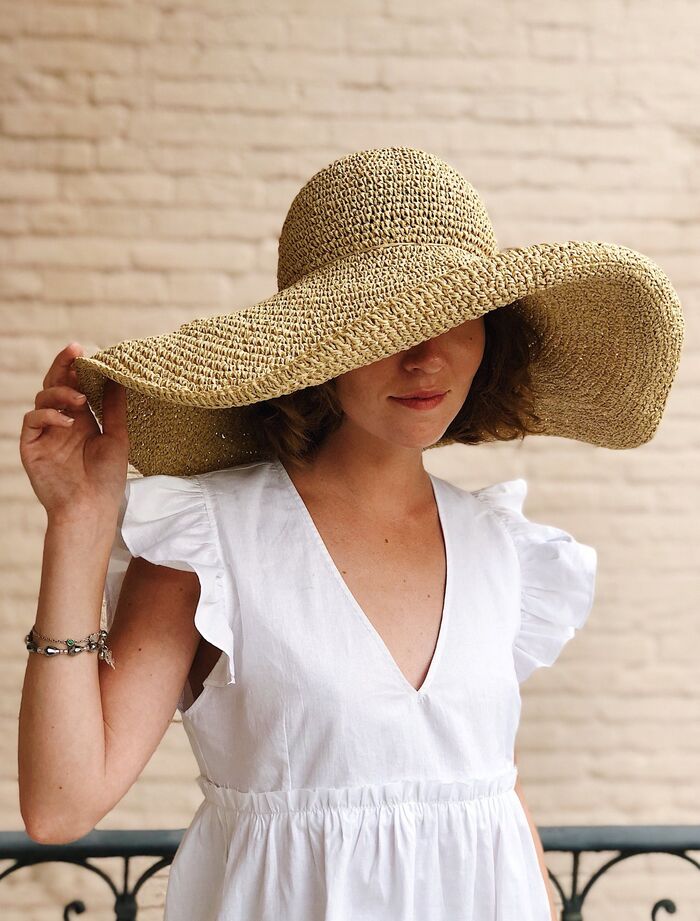 wide brim hat on a woman dressed in a white dress with a brick wall in the background