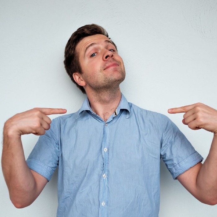 narcissist a man in a blue shirt pointing with two fingers towards himself and smiling