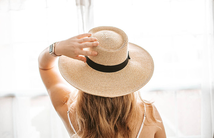 woman with her back to the camera with long hair and a watch holding her hat with wide trip and black accent