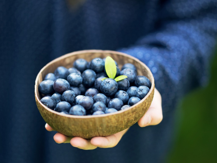 woman dressed in blue holding organic blueberries in a wooden bowl in her hand