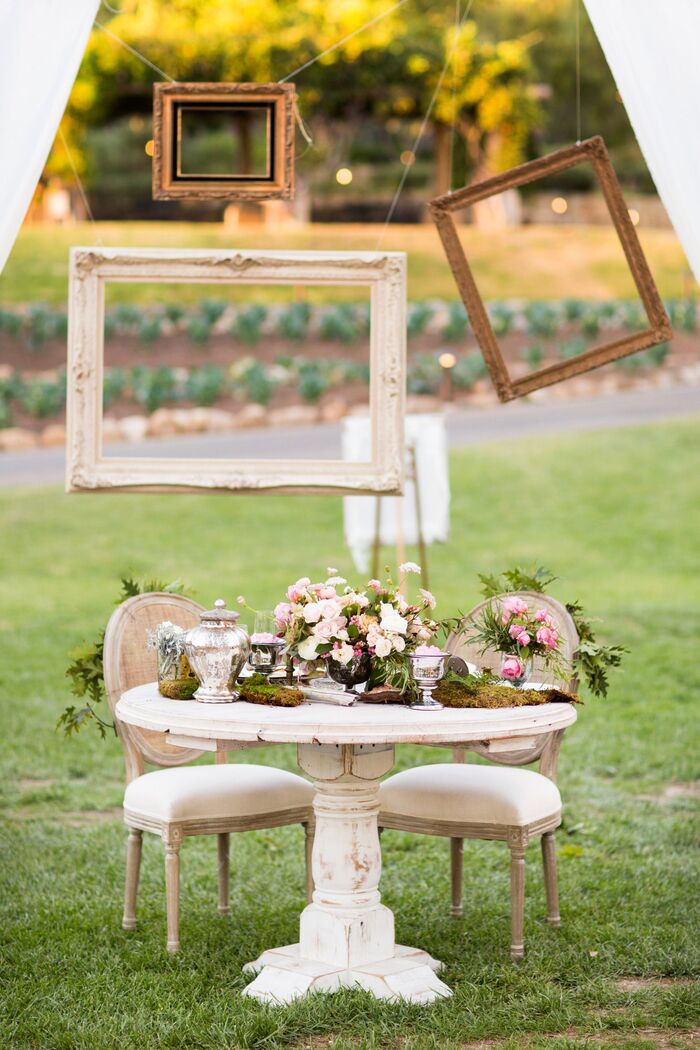 outdoor frames party decorations white table with two chairs flower arrangements and frames hanging in the background