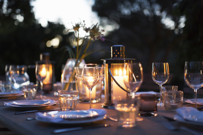 Candles in lanterns on patio dining table with place settings candle lit dinner with wine glasses and plates