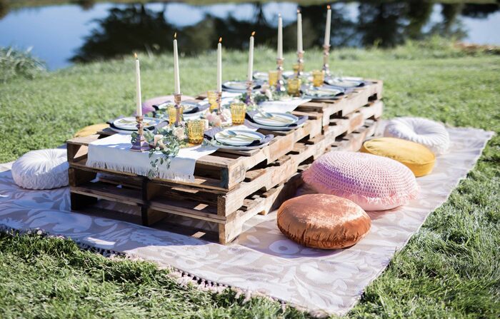 palette tables arranged for a garden party with pillows for sitting high candles and lake in the background