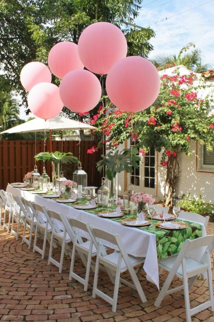 pink party balloons long white table with white chairs in a little yard with flowering plants