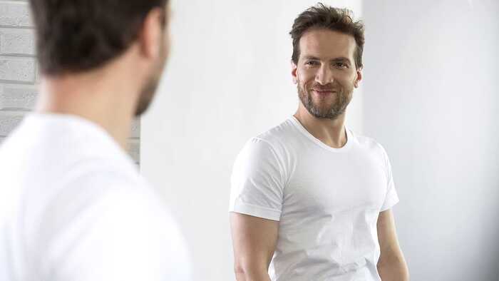 personality disorder narcissism a man in a white shirt looking at himself in the mirror and smiling
