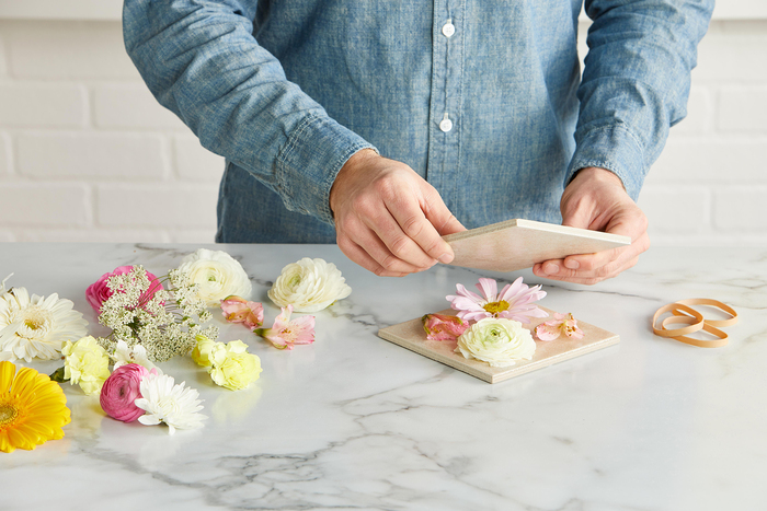 man in a denim blue shirt pressing different flowers on a marble countertop 