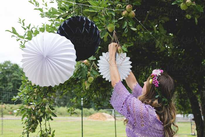 romantic summer party decor woman in purple dress decorating outdoors with large paper rosettes