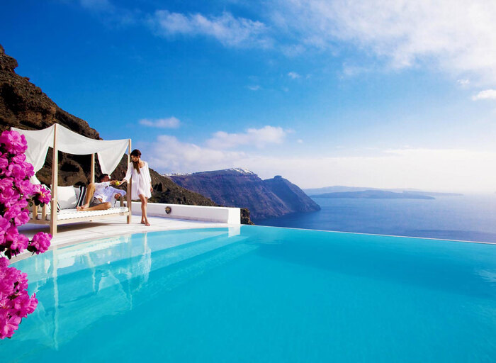 santorini infinity pool with couple relaxing next to it overlooking the sea and the islands