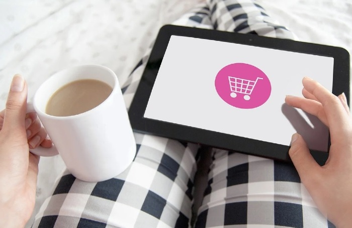 woman in checkered pants holding a coffee mug and a tablet shopping on the internet