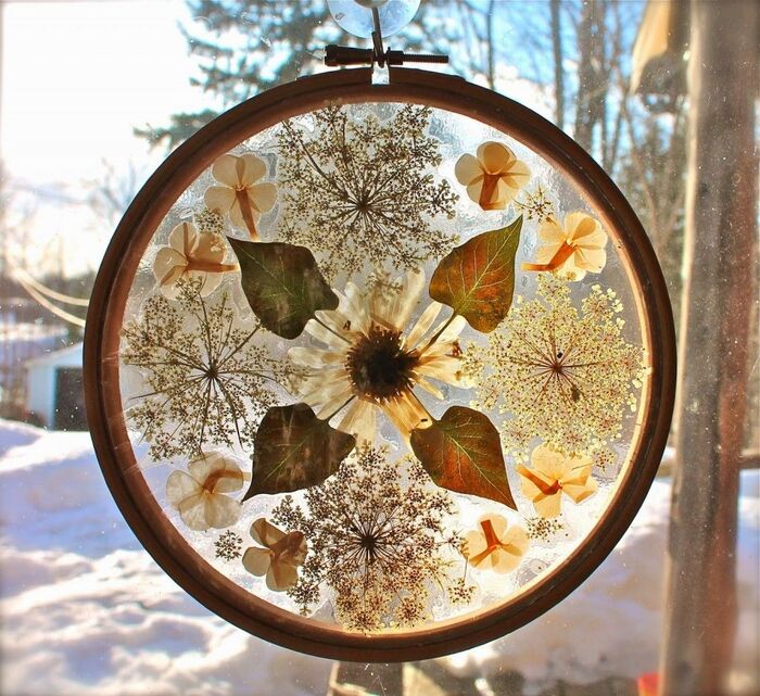 sun catcher with dried flowers hanging on a window with a winter landscape in the background