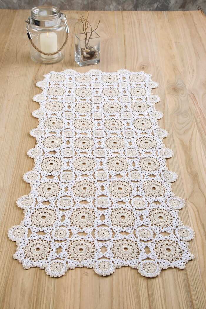 white table runner with granny crochet square patterns on a light wooden table