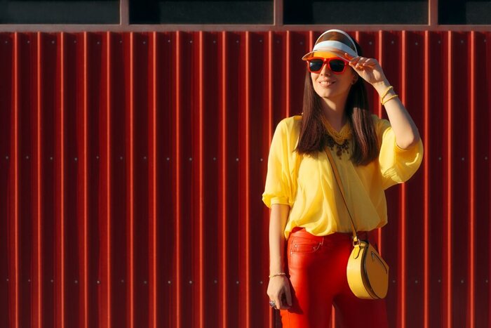 woman wearing visors yellow shirt and red pants with red sunglasses on a red wall