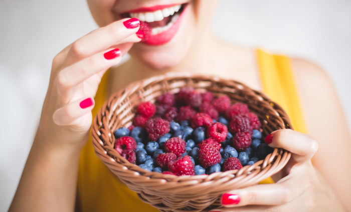 woman in yellow dress with red nail polish and red lipstick eating different berries from a basket