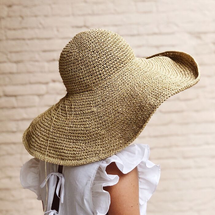 woman wearing a wide brim summer hat with a brick wall in the background 