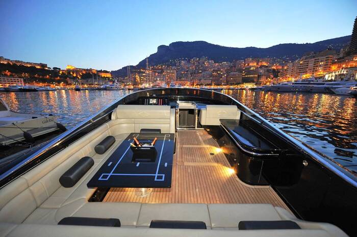 yachts of Monaco luxury yacht deck with wood and leather furniture party table and evening lights in the background