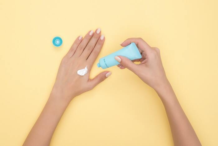 applying sun protection cream on the back of the hands on a yellow background from a light blue tube