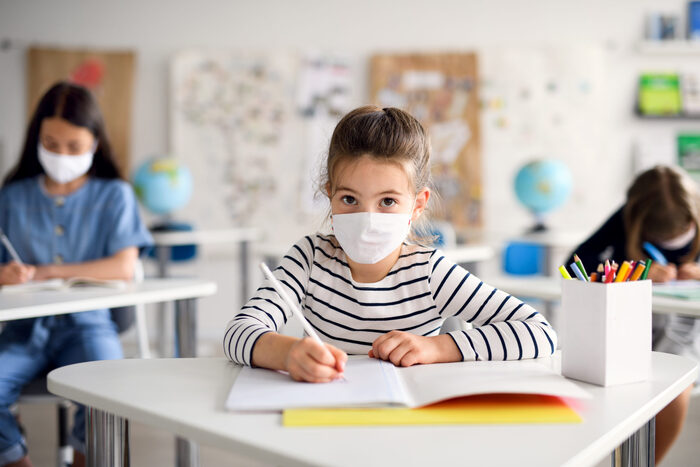 Back to school in pandemic with children with masks sitting in school on their desks and writing in their notebooks little girl in a striped shirt 