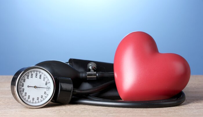 blood pressure measuring device on a wooden surface and a light blue background and a large red heart