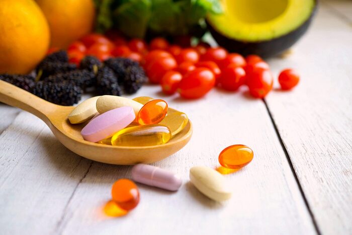 antioxidant supplements in a wooden spoon on a white table surface different color capsules and fruits in the background