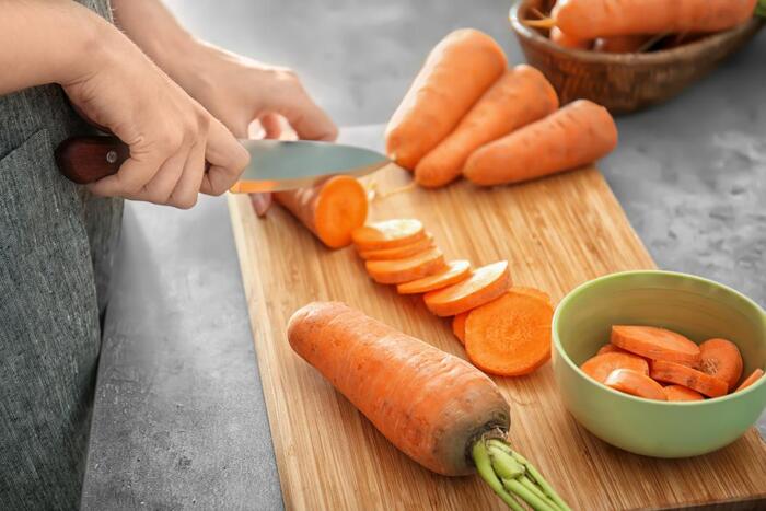 woman in a grey apron cutting carrots on a wooden cutting board in a kitchen