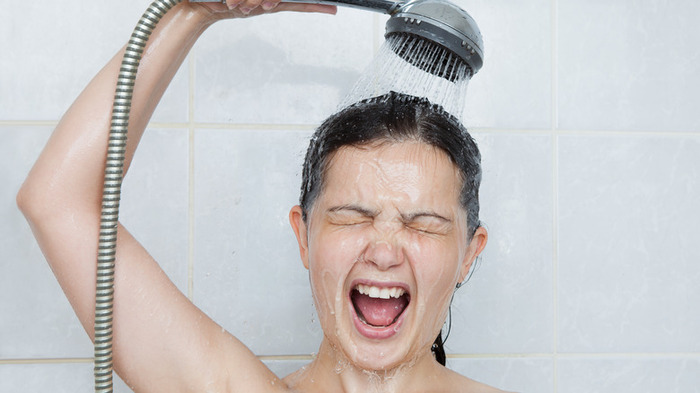 woman taking a cold shower in a white bathroom with a surprised face