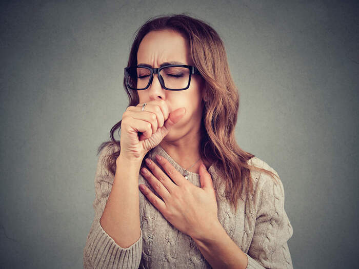 seasonal colds woman with black glasses in a beige sweater coughing in her hand