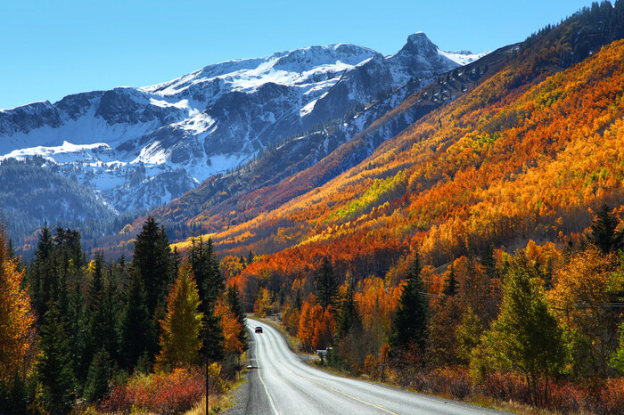 colorado road with a car on it and mountains with snowy peaks in the background fall slopes with colorful foliage