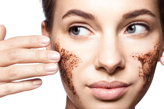 woman with blue eyes exfoliating her face with a brown sugar scrub touching her cheek with her hand