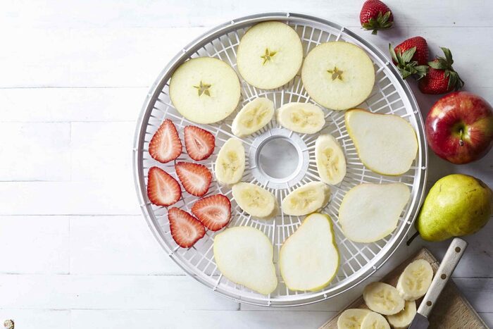 drying slices of different fruits in a food dehydrator on a white surface apple pear strawberries and slicing of bananas