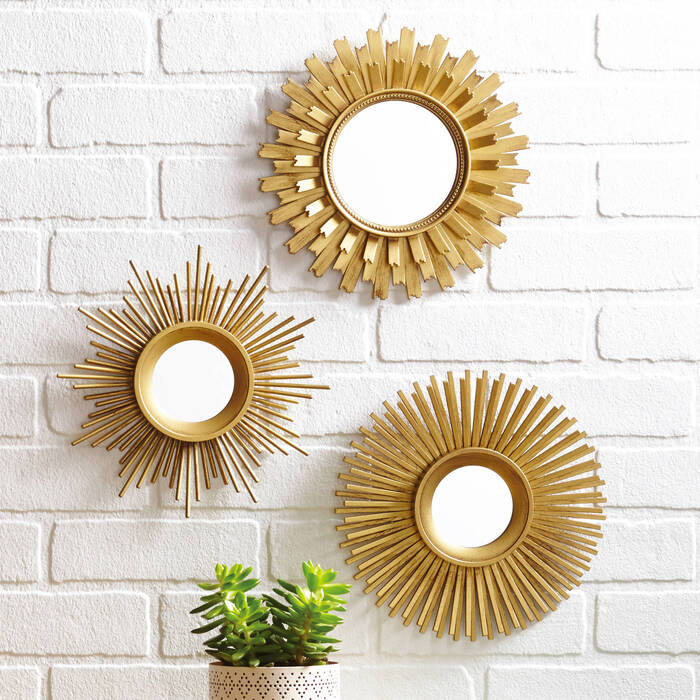 three hallway mirrors in golden frames on a white brick wall and a living green plant in front