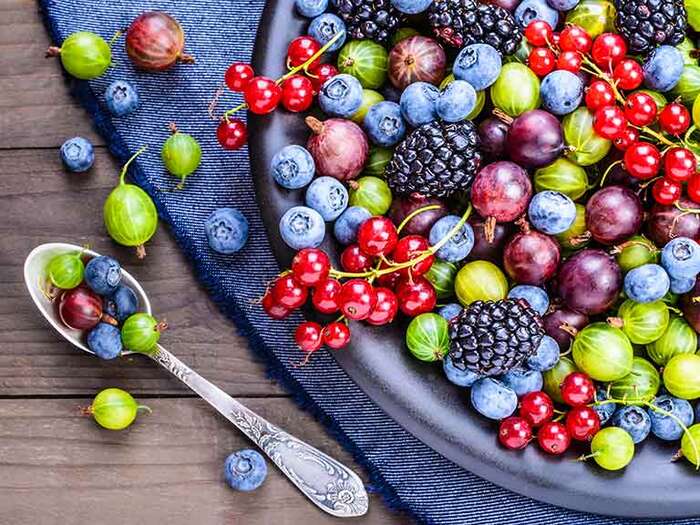 healthiest berries a large bowl with different berries on a table with blue table cloth and a tea spoon