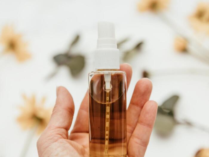 hand holding a homemade serum with light brown color on a floral background