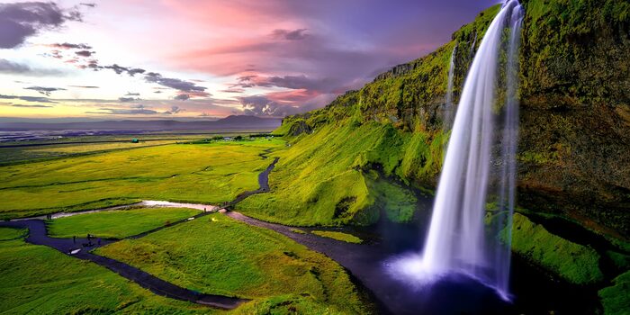 iceland eco tours waterfall with blue and white water falling from rocks covered in moss onto a green plain