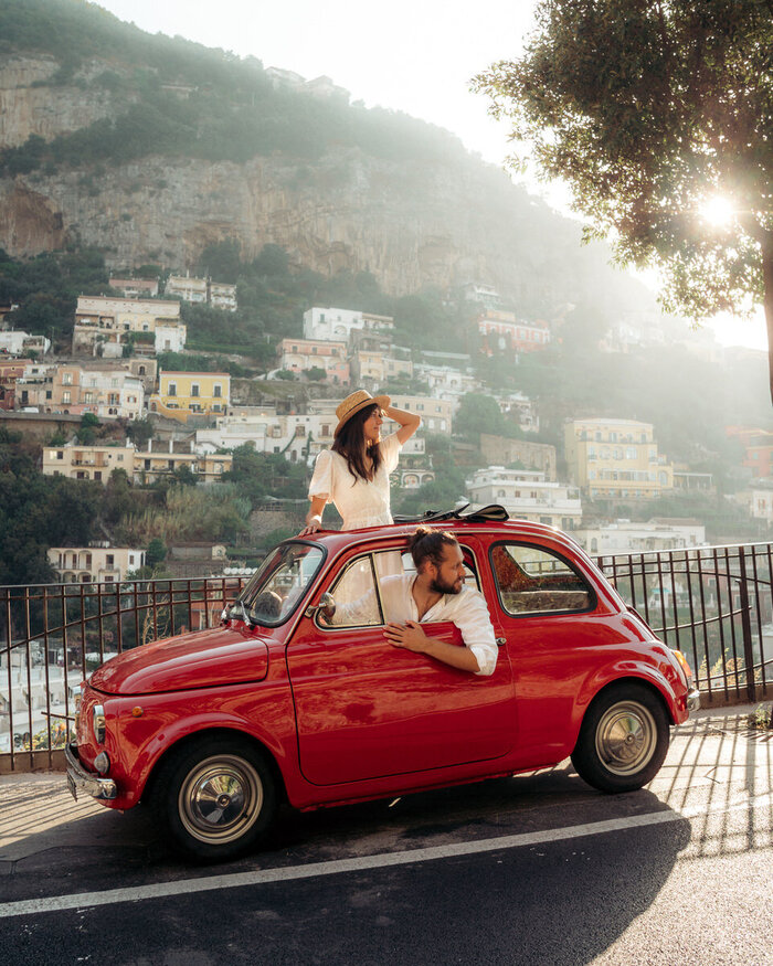 italian trip a couple in a small red mini car looking behind driving down the Amalfi coast