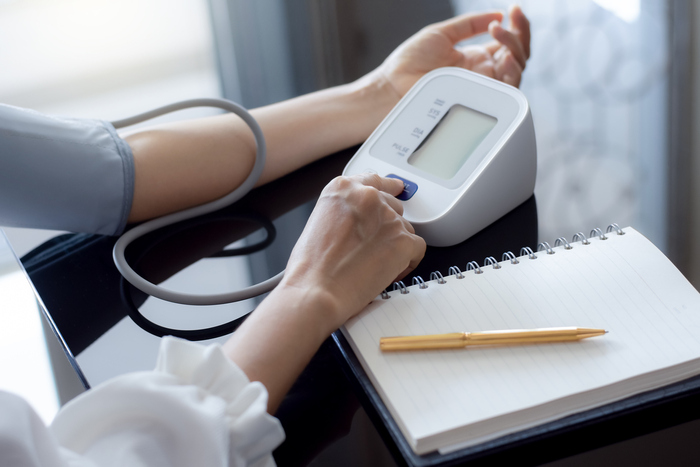 woman measuring blood pressure with on a dark table with a notebook and a pen next to her