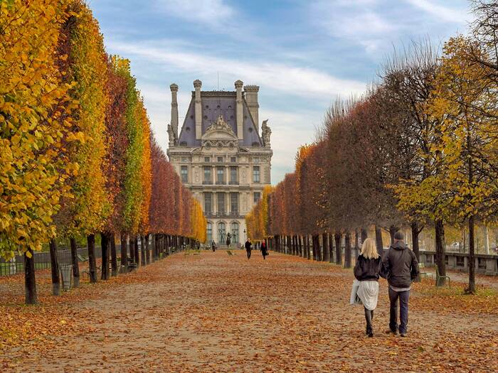 couple walking in Paris in fall colorful tress along an alley and a castle in the background